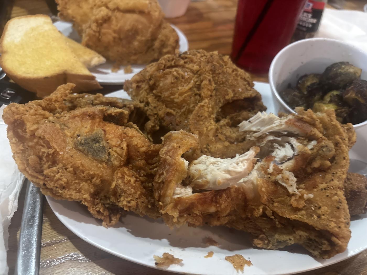 Bone-in fried chicken broken open, with Texas toast and Brussels sprouts