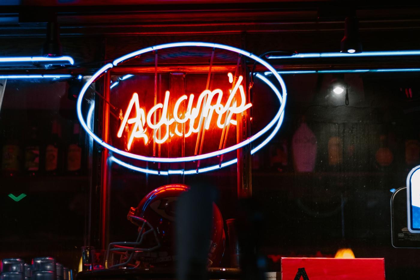 The red neon Adam's sign above the bar, with glassware and bottles behind it