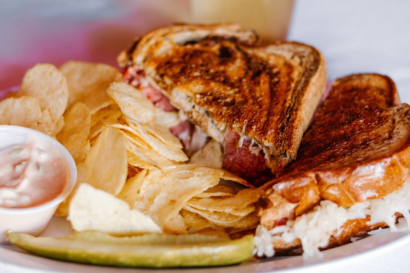 A reuben on marbled rye with sauerkraut, chips and a pickle spear